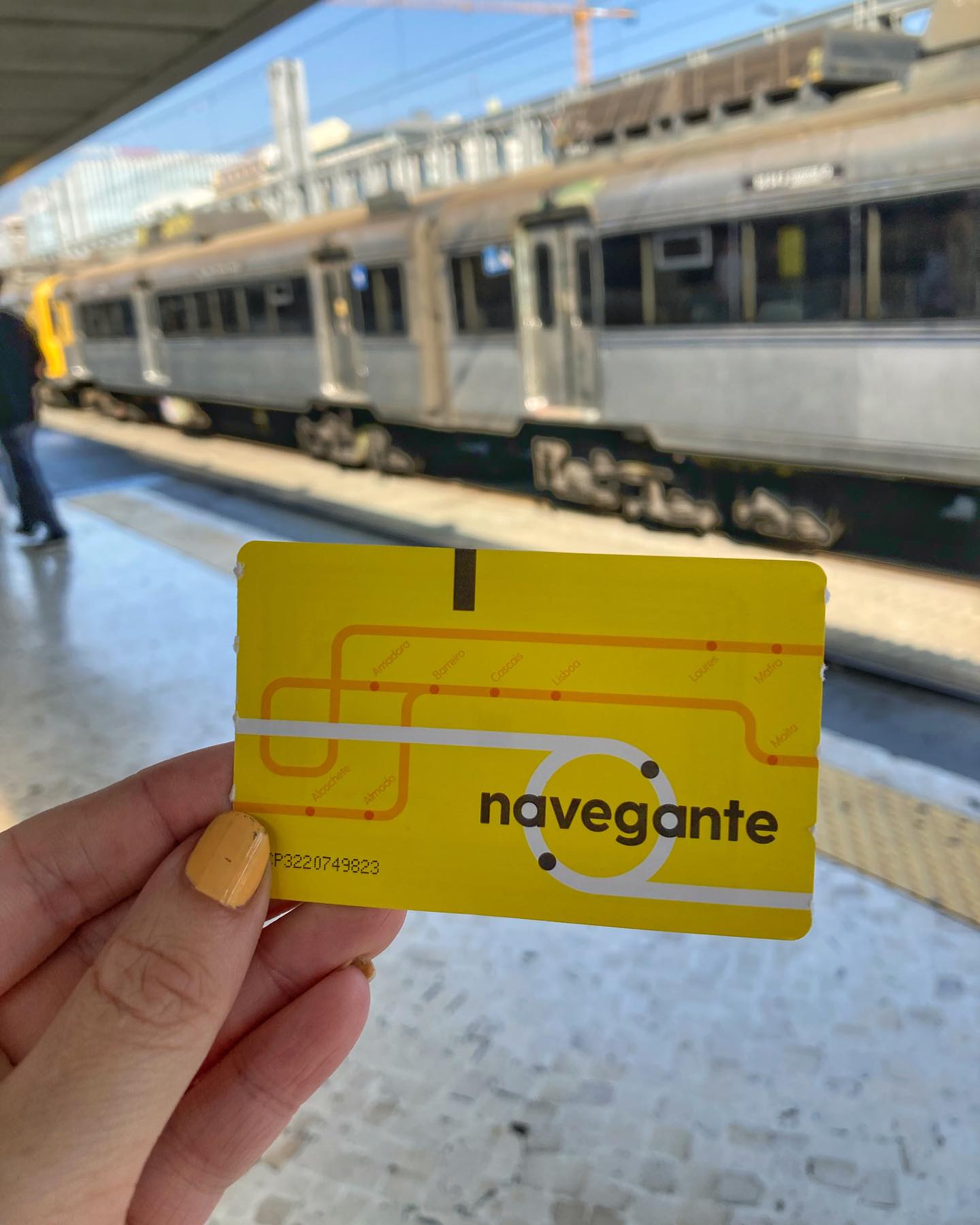 An image of a Navegante Card held in front of a train at Lisbon station, showcasing an affordable way to explore Lisbon using public transportation.