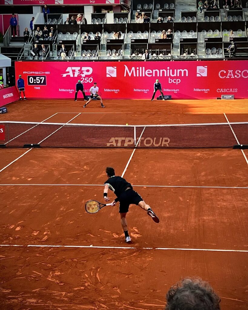 Lisbon in April: The Perfect Time To Visit 5 Exciting tennis match at Lisbon's outdoor clay courts during April, showcasing top players competing in a vibrant atmosphere with spectators and scenic city views.