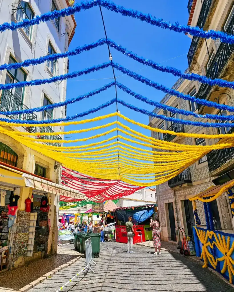 St Anthony Festival Lisbon: 4 Best Events and Traditions 2 Colorful street decorations with yellow, red, and blue streamers in a lively Lisbon neighborhood during a local festival.