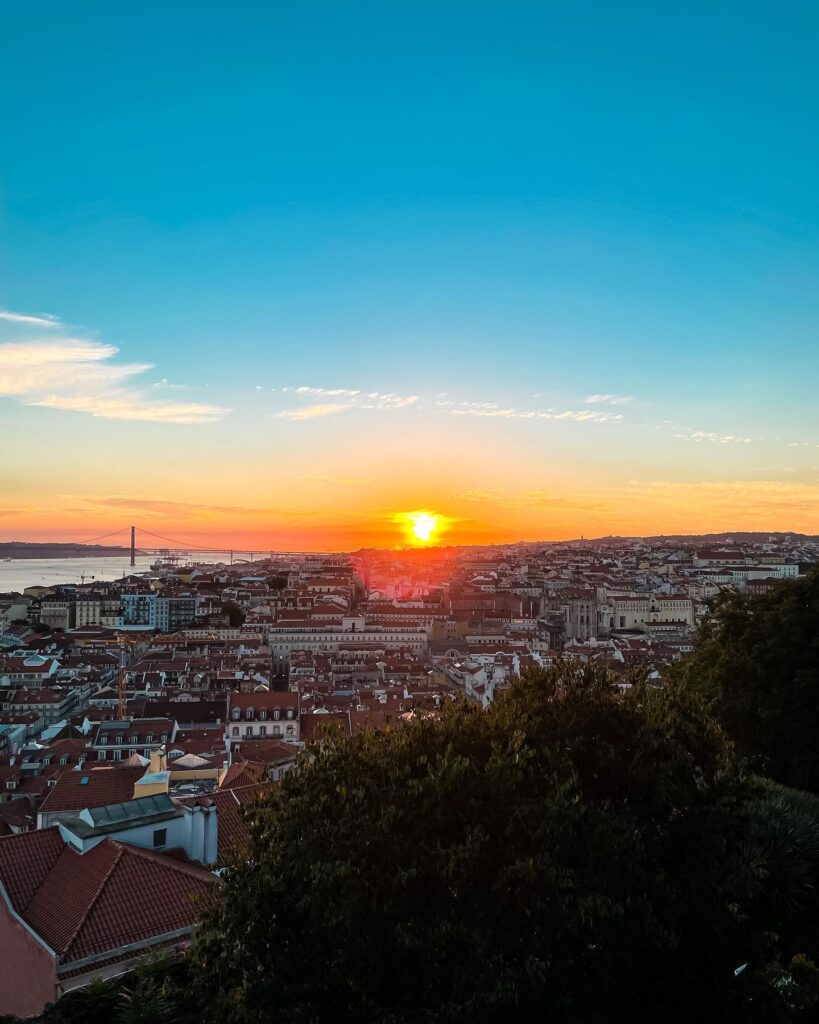 Beautiful sunset view of Lisbon during autumn, showcasing vibrant city rooftops and the Tagus River in the background, perfect for fall travel inspiration.