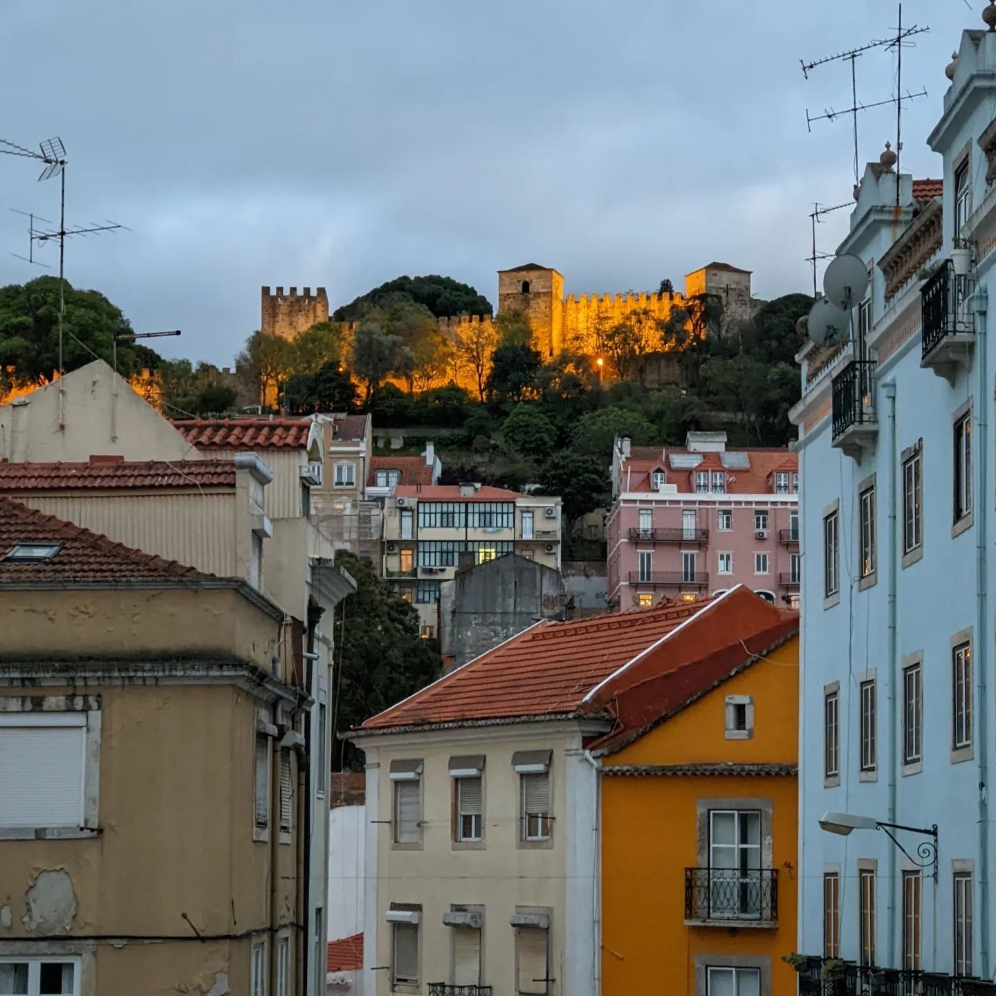Lisbon in April: The Perfect Time To Visit 1 Scenic view of Lisbon's historic castle illuminated at sunset, overlooking colorful city buildings and the vibrant neighborhood below.