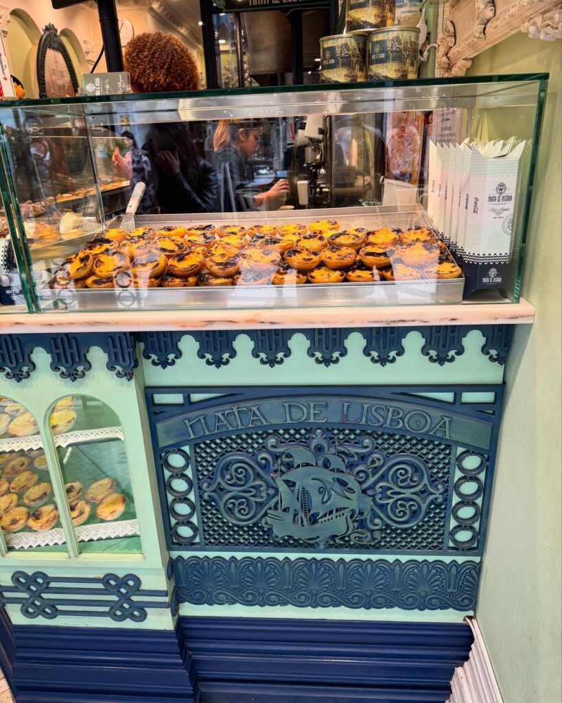 Crispy pastel de nata pastries in display case at Lisbon bakery, traditional Portuguese dessert, LisbonVibes, decorated vintage-style bakery, authentic Lisbon sweets, Portuguese pastry shop, iconic Lisboa treats, Lisbon culinary experience.