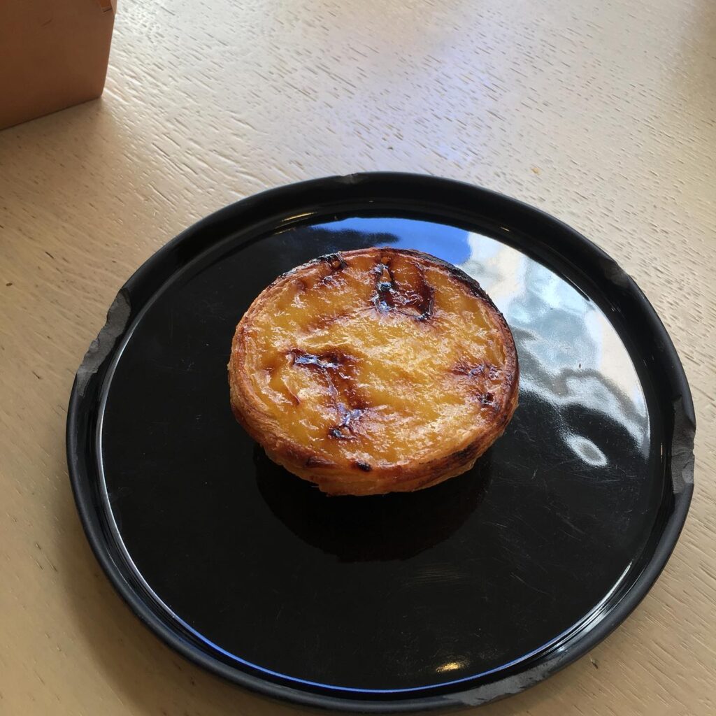 Golden Portuguese egg tart pastry on black plate at LisboaVibes, showcasing authentic Lisbon desserts. Perfect for exploring Lisbon's rich pastry culture and culinary delights. Located in Lisbon, Portugal.
