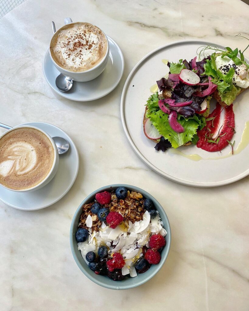 Lisbon in May - Less Crowded? (Perfect Time To Visit) 2 Bright coffee cups with frothy cappuccinos and a vibrant mixed greens salad on a white plate.