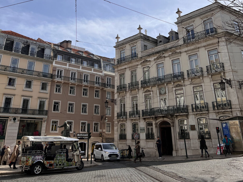 Historic buildings and lively street scene in Lisbon, Portugal, showcasing classic architecture, local shops, and pedestrians enjoying a vibrant city atmosphere.