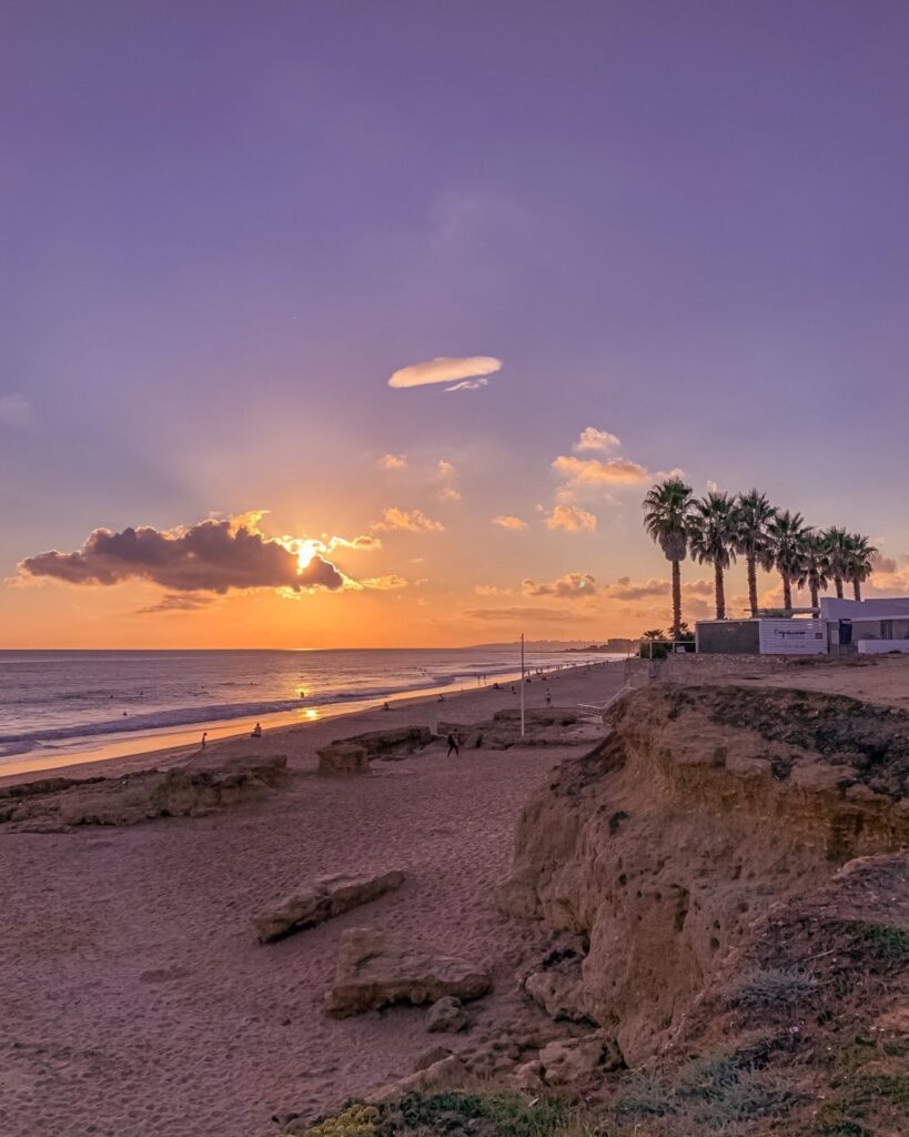 Beautiful sunset over Lisbon's beach featuring palm trees, sandy shores, and rocky cliffs, perfect for relaxing and enjoying scenic coastal views in Portugal.