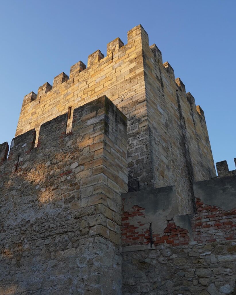 Historic fortress wall in Alfama, Lisbon, showcasing medieval architecture and stone construction with battlements under a clear blue sky.