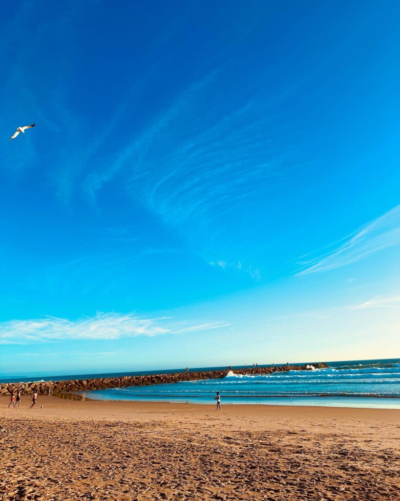 Relaxing Lisbon beach with golden sands, calm waters, and a clear blue sky, ideal for sunbathing, swimming, and seaside activities.
