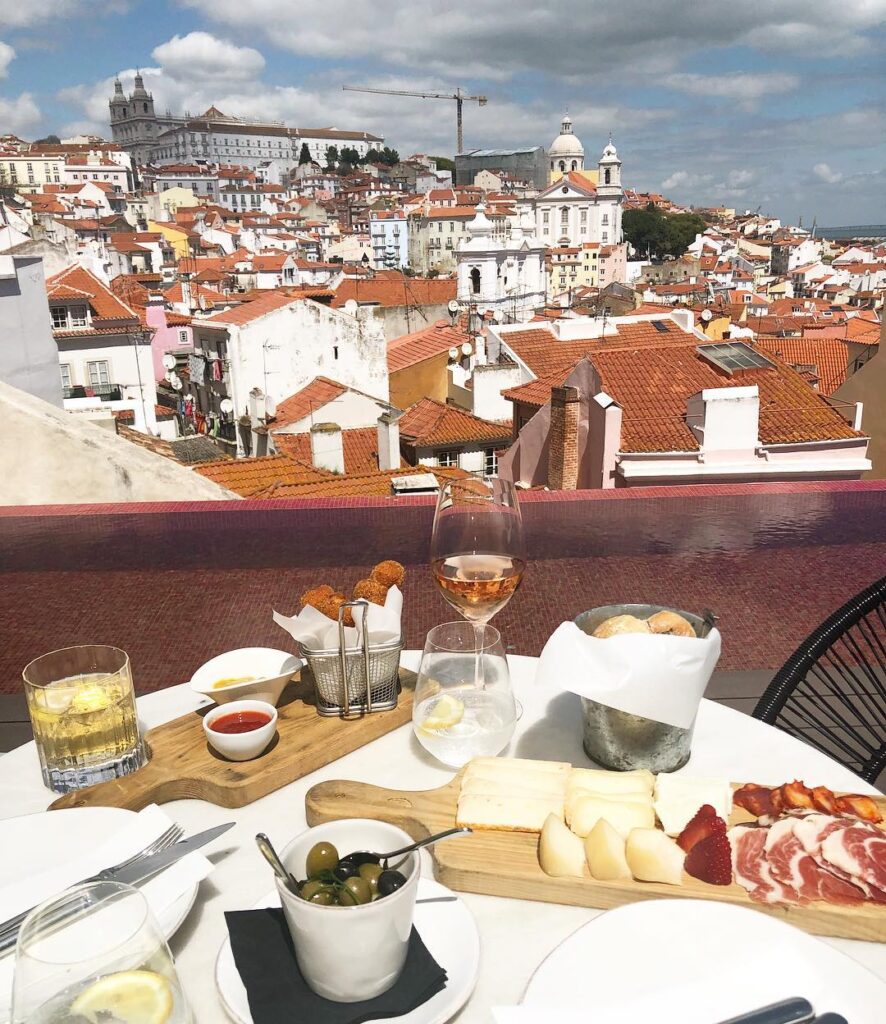 Alfama in Lisbon: A tourist enjoying a meal with a panoramic view of the historic Alfama district, featuring colorful rooftops and iconic landmarks in the background.