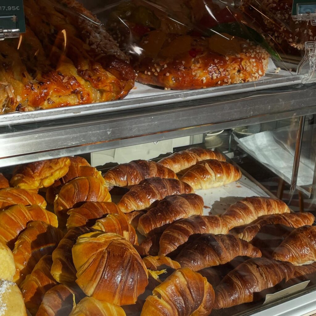 Buttery croissants and assorted pastries in a bakery display case in Lisbon, Portugal, showcasing delicious baked goods, perfect for breakfast or a snack during LisbonVibes exploration.