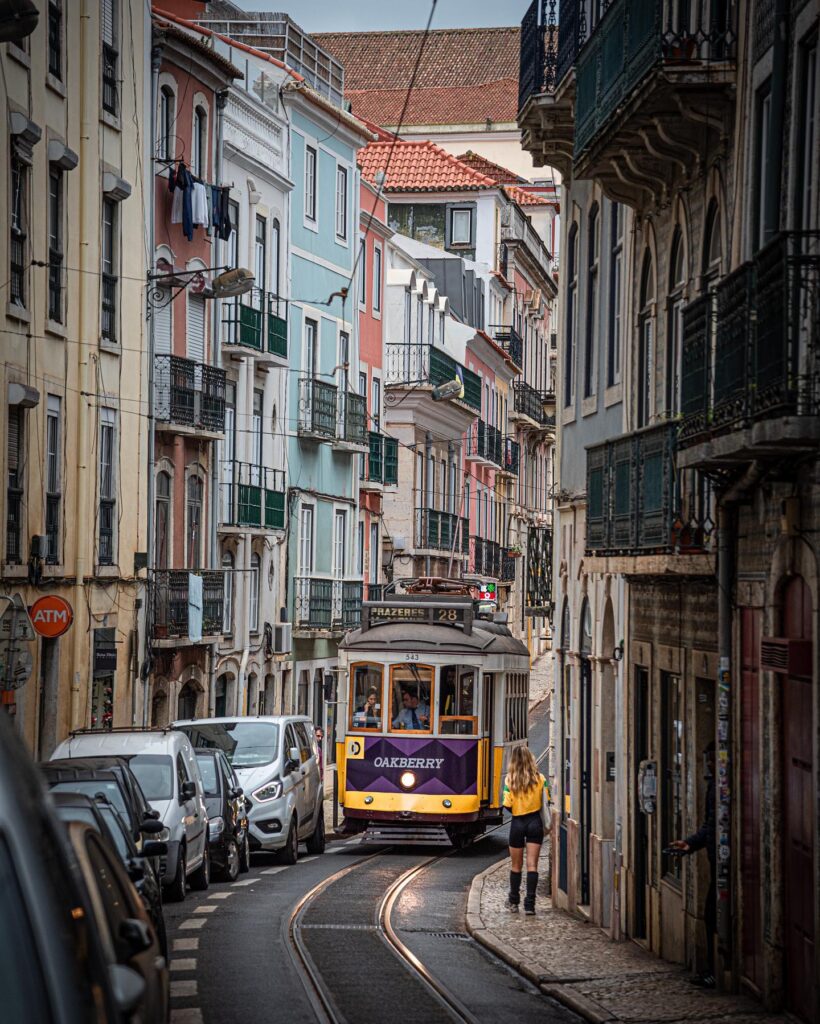 Historic Lisbon Tram 28 navigating narrow streets with colorful buildings in the Alfama district, showcasing iconic Portuguese transportation and vibrant city scenery.
