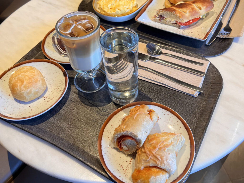 Lisbon Food Guide: What to Eat + Where to Eat (Local Tips + Map) 3 Creamy iced coffee with milk, fresh water, and traditional Portuguese pastries including spring rolls and breaded snacks served on a stylish breakfast tray in Lisbon.