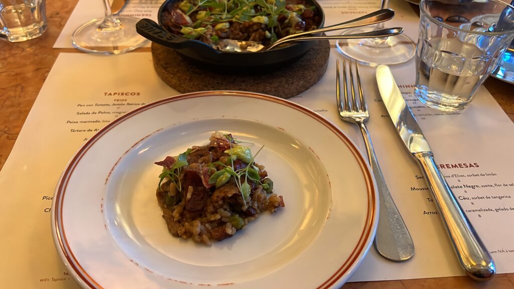1. Delicious Portuguese-style rice dish with fresh greens and tender meat, served elegantly on a vintage plate at a Lisbon restaurant.