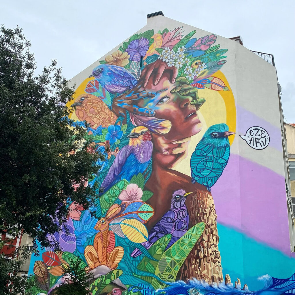 Colorful mural depicting a woman with a floral headdress and birds in Graça neighborhood, Lisbon, showcasing urban art and local culture.
